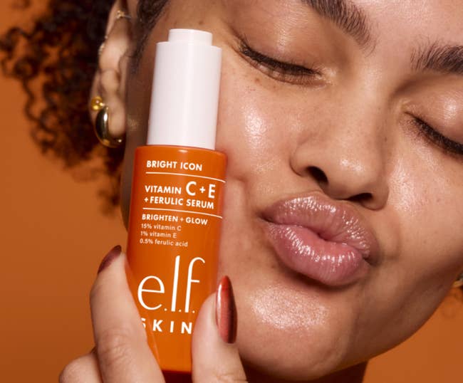 Model with closed eyes and glossy lips holding e.l.f. Vitamin C+E serum bottle, suggesting skincare merchandise  usage