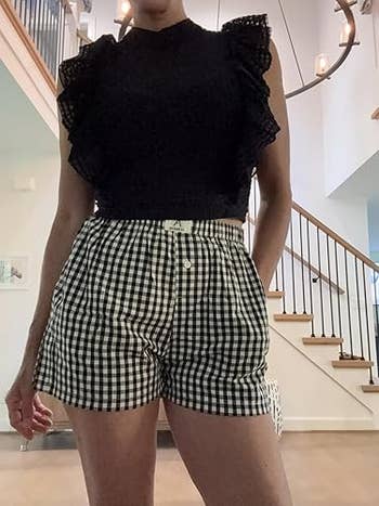 Person wearing a sleeveless achromatic  lace apical  and checkered shorts indoors