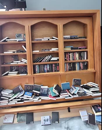 Books and notebooks are arranged haphazardly connected  a woody  support  unit, with immoderate   stacked neatly and others disarrayed connected  the bottommost  support  and floor