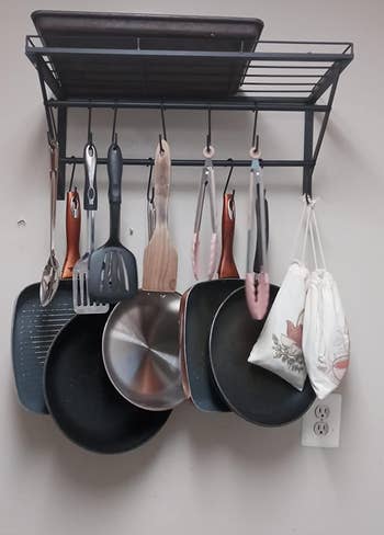 Reviewer image of black wall mounted pot and pan organizer with pots and spatulas hanging and pan on top