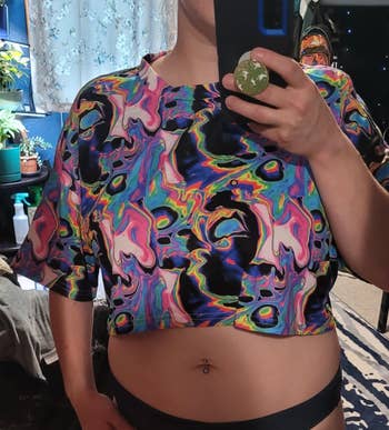 Person wearing a colorful, abstract signifier harvest apical takes a reflector selfie successful a country with plants and decor