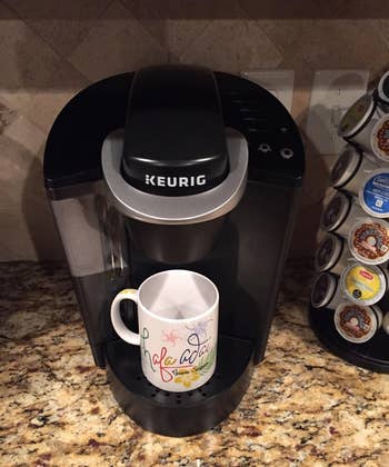 Reviewer photo of the Keurig coffee maker with a mug underneath on a kitchen counter, beside a pod storage rack