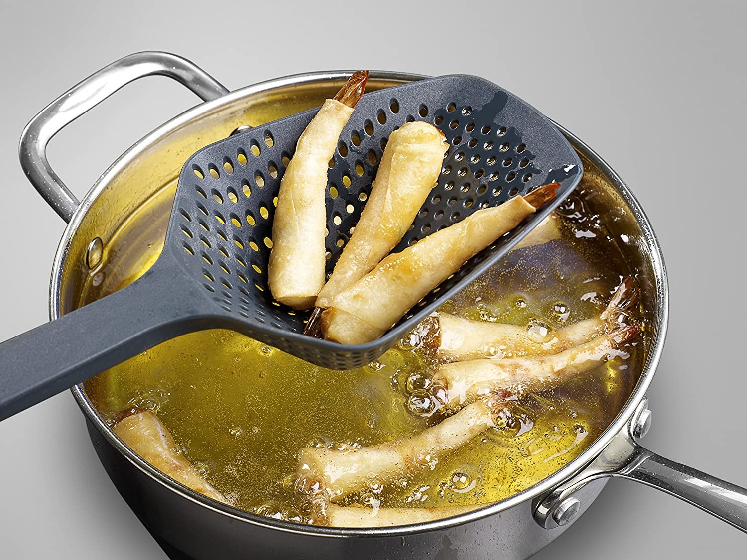 A black scoop with small colander holes in it plucking fried shrimp out of a pot