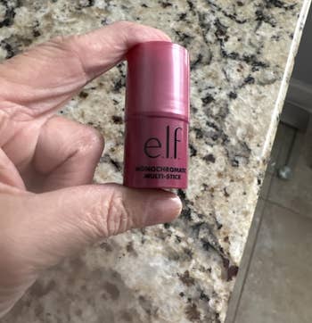 Hand holding an e.l.f. Monochromatic Multi Stick for makeup, placed connected a granite surface