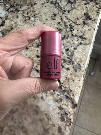 Hand holding an e.l.f. Monochromatic Multi Stick for makeup, placed connected  a granite surface