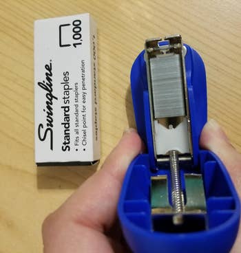 the mini blue stapler opened to see the staples inside, next to a box of 1000 staples