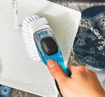 Hand holding a scrub brush cleaning a white plate under running water