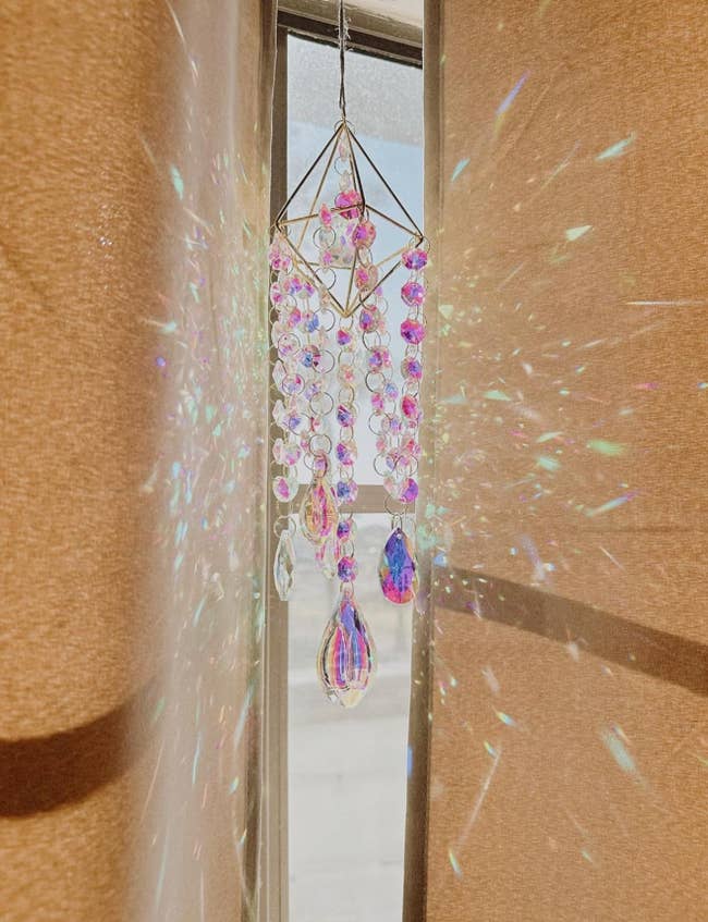 Hanging crystal prism with beads casting colorful airy  reflections done  a sheer curtain successful  a sunlit room. Popular location  decor item