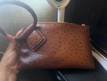 Hand holding a textured leather wristlet bag with a looped handle, suitable for fashion and shopping articles