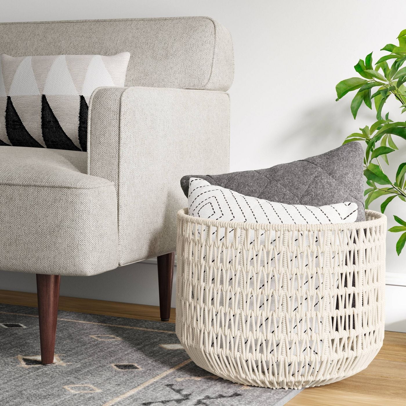 the woven rope basket in white sitting next to a couch with pillows in it