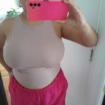 Person taking a mirror selfie, wearing a sleeveless fitted top and loose pants