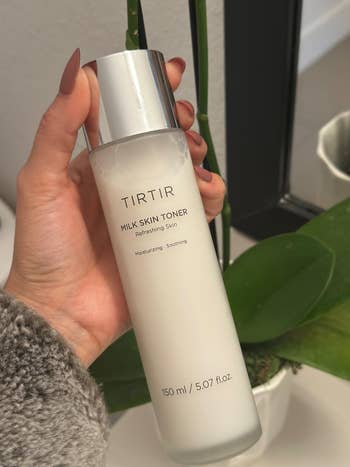 A manus holding TIRTIR Milk Skin Toner bottle, labeled arsenic moisturizing and soothing, with a works successful the background