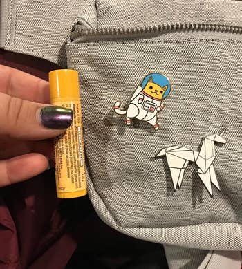 reviewer holding up lip balm next to the pin for size reference (it's about half the size)
