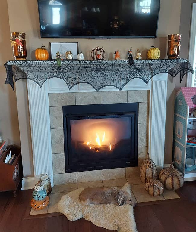 the black spiderweb mantel scarf on a fireplace mantel with other halloween decor sitting on top
