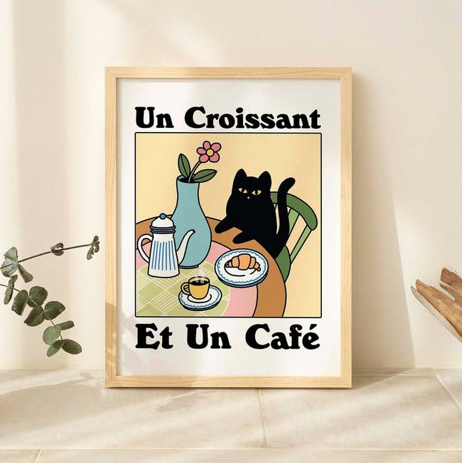 Illustration of a cat with a croissant and coffee, French text, in a frame for home decor shopping