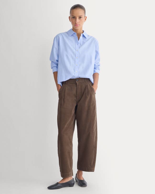 Person successful  a casual outfit with a relaxed-fit button-up garment  and wide-leg trousers, hands successful  pockets, lasting  against a plain background
