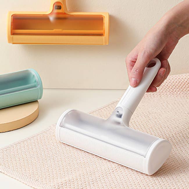 Hand using a lint roller on a fabric surface, with other rollers in the background; image related to home cleaning products