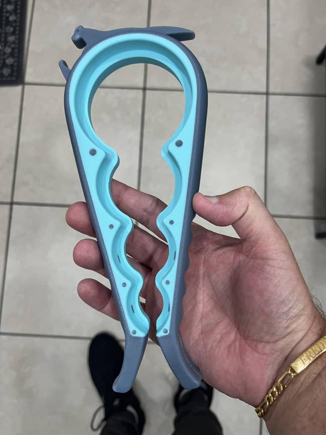 Hand holding a multi-function jar opener connected  a tiled floor, highlighting its easiness  of usage  for assorted  lid sizes