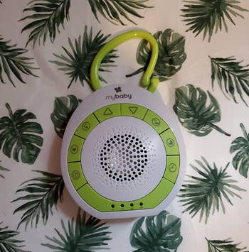 Portable baby sound machine with buttons and a speaker, hanging against a leaf-patterned background