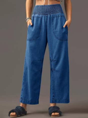 Person wearing high-waisted, wide-leg denim pants and fuzzy sandals, lasting  with hands successful  pockets, showcasing casual style