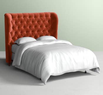 Orange velvet tufted headboard with wings on the side attached to a white bed
