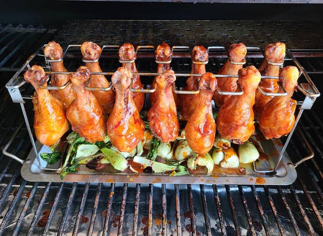 marinated chicken wings hanging from a rack over a metal tray full of veggies 