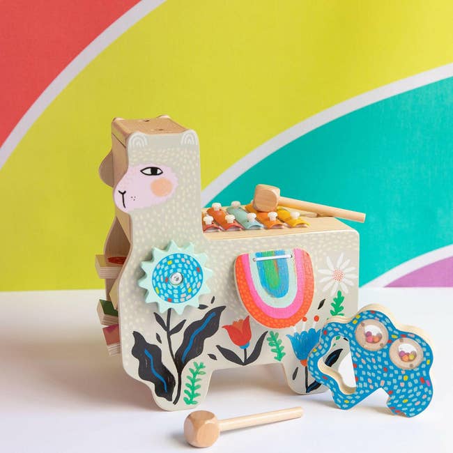 Llama-shaped xylophone artifact with colorful keys, floral patterns, and woody mallets, acceptable against a rainbow backdrop
