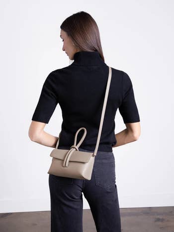 Woman in a black turtleneck and jeans with a beige crossbody bag