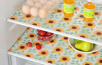 Sunflower-patterned shelf liners in a fridge with bottled mango juice, a bowl of tomatoes, eggs, and pears