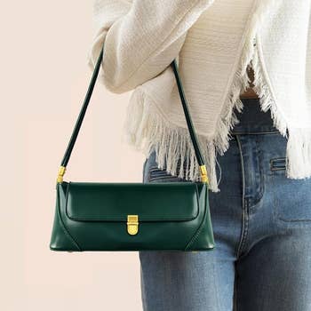 Model holding the strap of a dark green small baguette style purse with gold clasp 