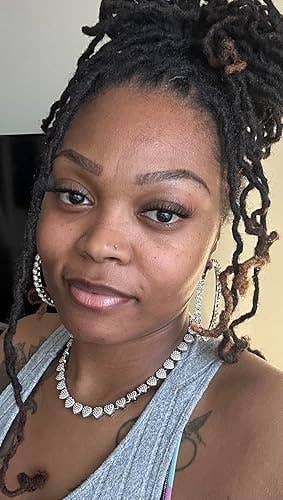Person smiling, wearing hoop earrings and a pearl necklace with braids pulled up