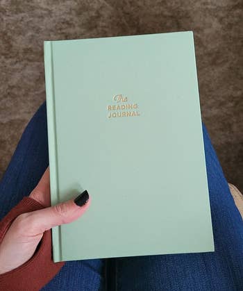 reviewer holding a green hardback journal with gold embossed print that says 