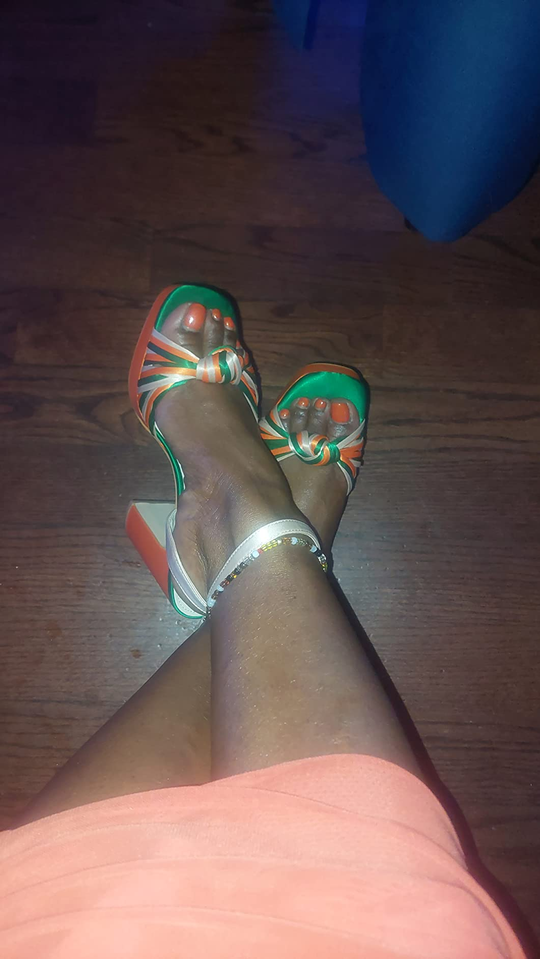 Person wearing striped high-heeled sandals and a beaded ankle bracelet, sitting connected  a woody  floor