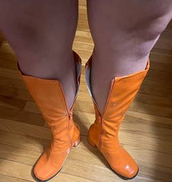 reviewer showing a pair of knee-high boots that don't fit around their calves