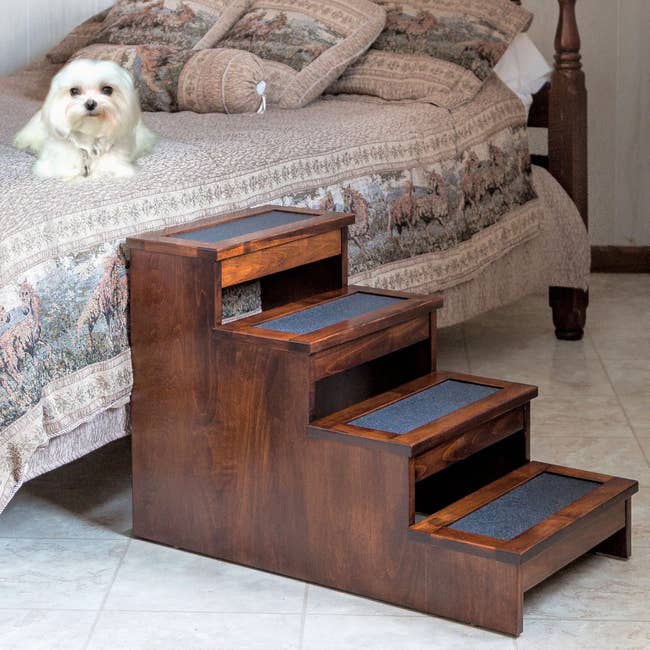 Wooden and black four-step stairs up against bed on tile flooring and dog lying on top of bed
