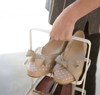 Person carrying a footwear  rack with beige polka dot flats featuring bows, alongside different  brace  of shoes. Shopping theme