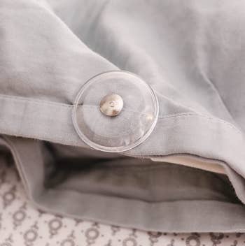 a clear circular pin pressed into a duvet cover pinning the duvet in place 