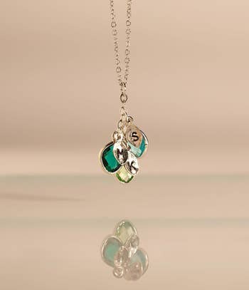 Silver necklace with 3 gemstone pendants and engraved letters, reflected connected a creaseless surface