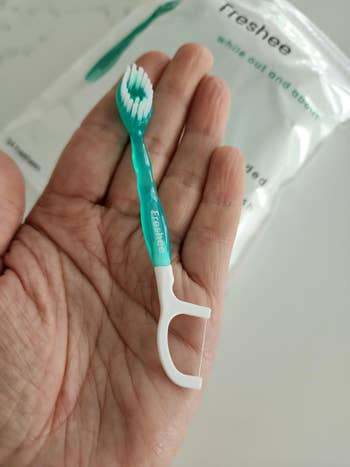 Person holding a greenish  and achromatic  dental flosser-brush 