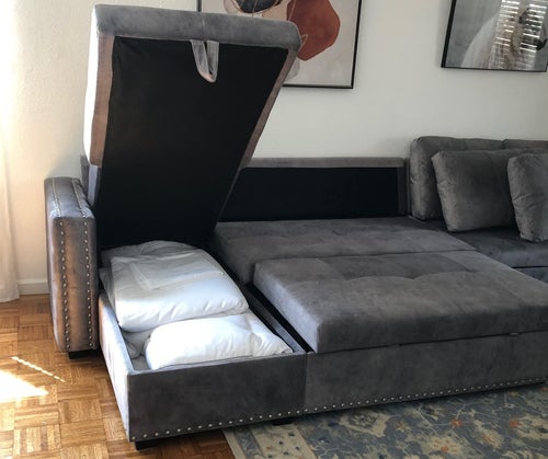 reviewer photo of couch in gray, folded out into sleeper, storage space exposed