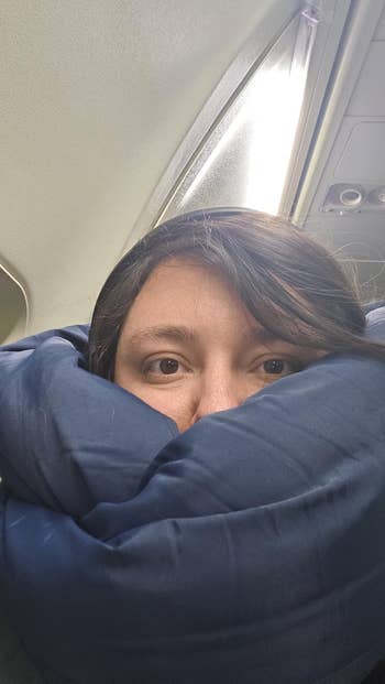 Person resting head on travel pillow by airplane window
