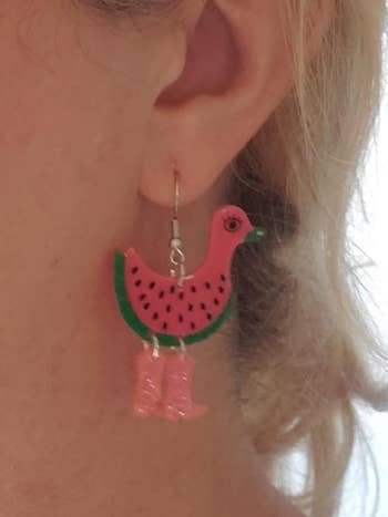 Person wearing a playful earring shaped like a bird with watermelon and pink cowboy boots