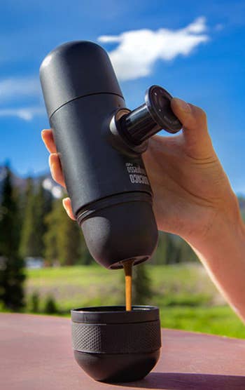 Portable espresso shaper  being utilized  outdoors, with java  pouring into a matching cup, acceptable   against a backdrop of trees and a wide   sky