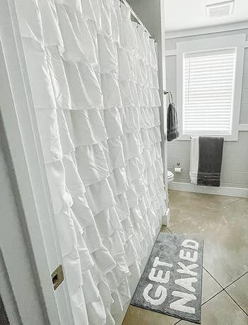 reviewer side-view photo of the white ruffled shower curtain in their bathroom