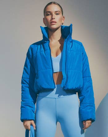a model wearing a sports bra and leggings with a bright blue cropped puffer jacket 