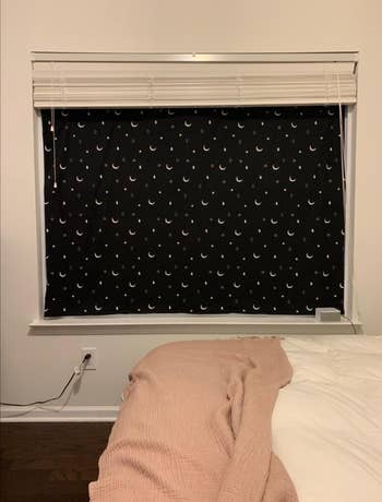 A blackout curtain with white moons and stars suctioned to a window, blocking the light 