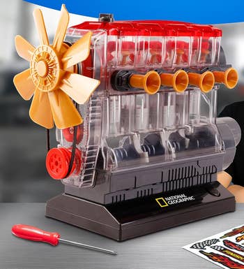 Teen assembling a transparent exemplary of a 4-cylinder motor with disposable moving parts, container includes stickers and a reddish screwdriver