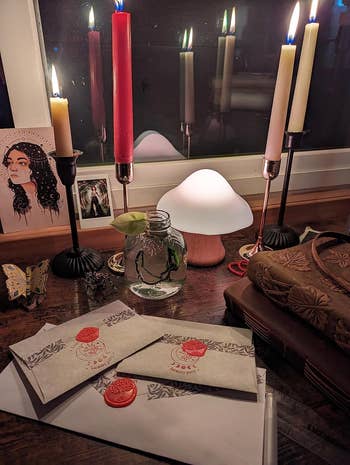 Cozy setup with candles, a mushroom lamp, sealed letters, and a jar with a works  cutting, creating a charming, cottagecore-inspired atmosphere