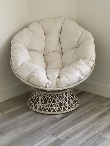 Reviewer image of white papan chair with white wicker stand and tufted plush matching cushion in front of a white wall