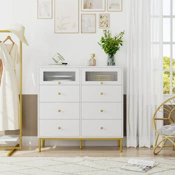 six-drawer white dresser with gold hardware as well as two compartments with clear windows